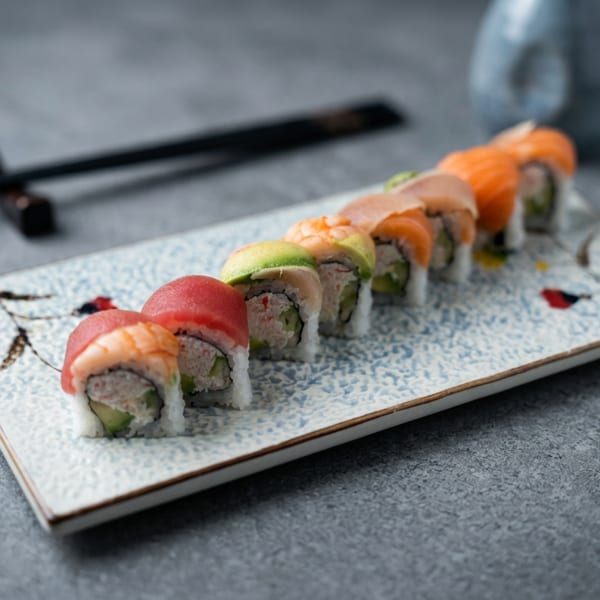 Colorful sushi rolls arranged on a rectangular ceramic plate with black chopsticks on a dark tabletop.
