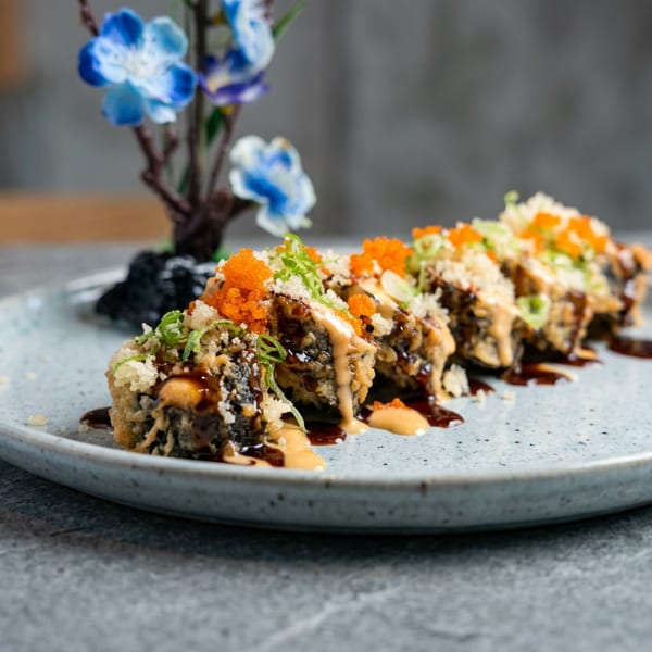 Tempura-fried sushi rolls topped with orange roe, scallions, crumbs, and sauces on a blue ceramic plate.