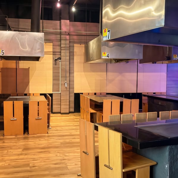 Empty hibachi restaurant with multiple teppanyaki tables, wooden chairs, and stainless steel exhaust hoods.