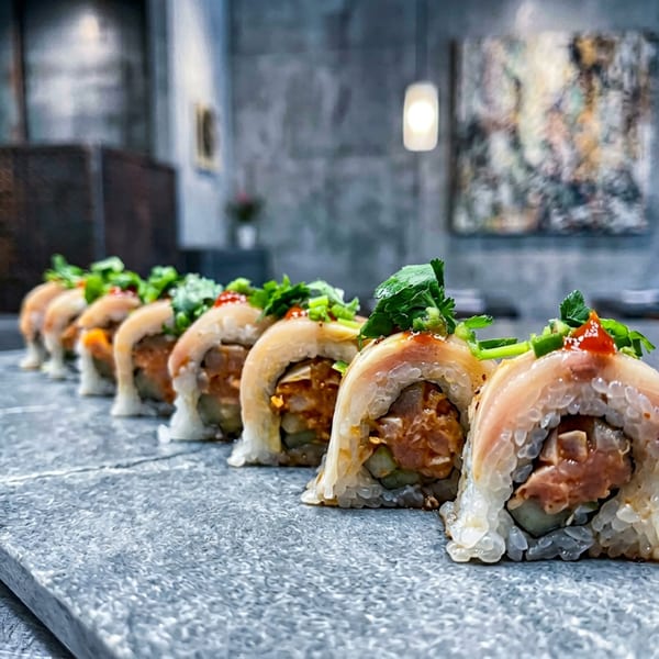 A row of sushi rolls with fish, rice, and green garnish on a textured gray surface.