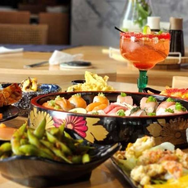A vibrant spread of Japanese dishes, including sushi, edamame, and a cocktail, on a wooden table.