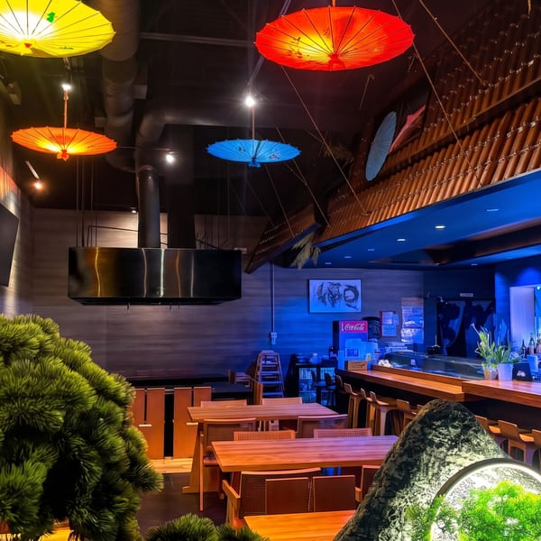 Asian-themed restaurant interior with vibrant paper umbrellas, wooden tables, and a blue-lit bar area.