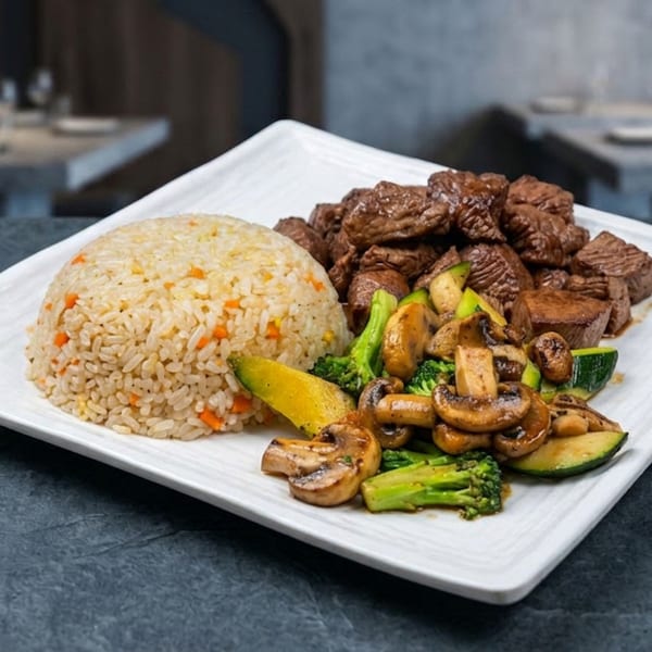 Hibachi steak with fried rice, broccoli, zucchini, and mushrooms on a white rectangular plate.