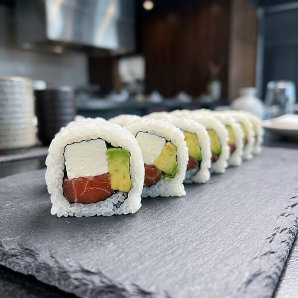 Sushi rolls with tuna, avocado, and cream cheese on a dark slate board in a restaurant setting.