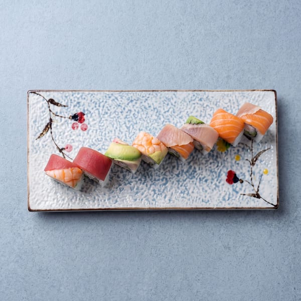 Colorful sushi rolls with tuna, shrimp, avocado, and salmon on a decorative rectangular plate.