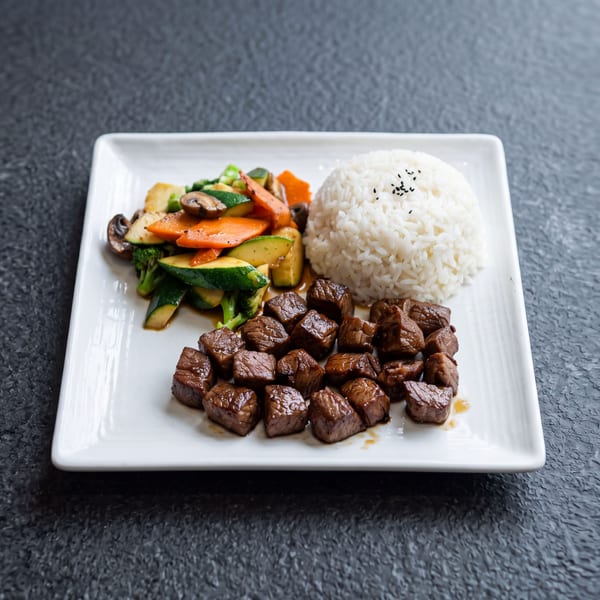 A white rectangular plate holds a meal of diced beef, white rice, and mixed stir-fried vegetables.