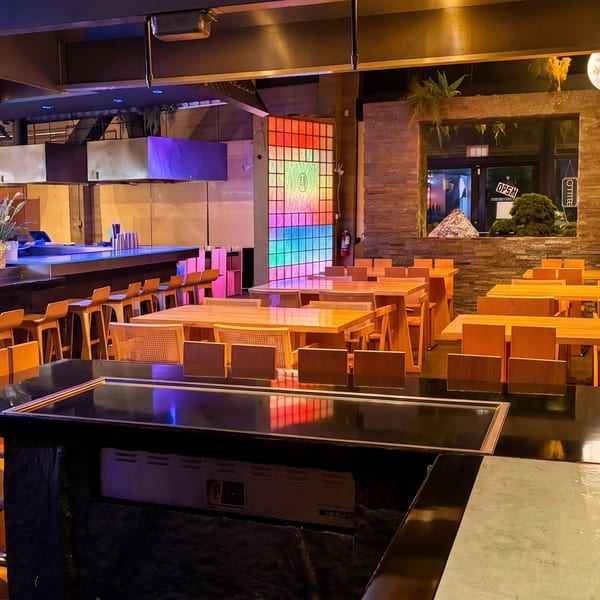 Sleek restaurant interior with a bar, wooden tables, and a vibrant, colorful illuminated wall.