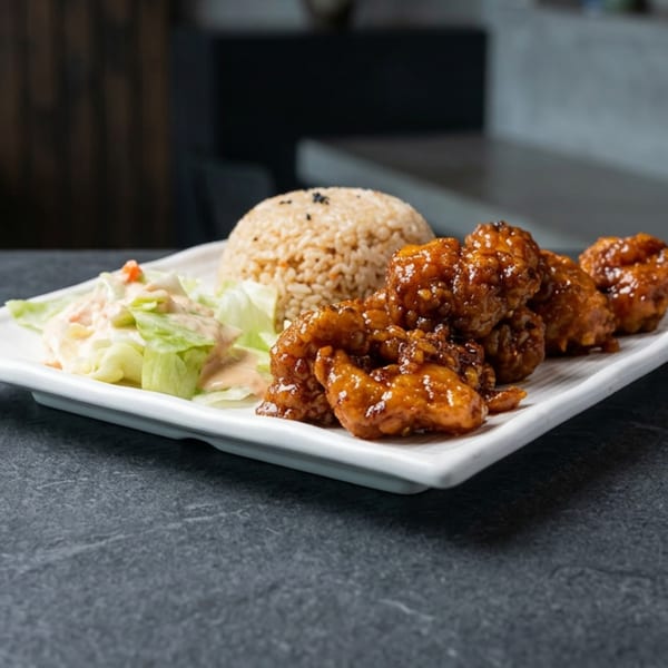 A white rectangular plate holds a serving of brown rice, glazed chicken, and a side salad.