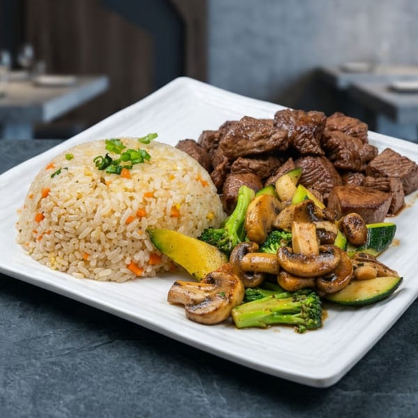 Hibachi steak, fried rice, and mixed vegetables including mushrooms, broccoli, and zucchini on a white plate.