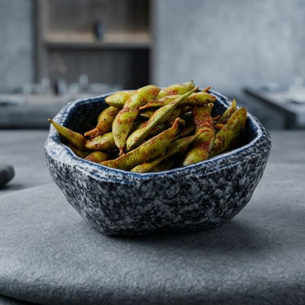 A stone bowl filled with seasoned edamame pods sits on a dark gray surface.