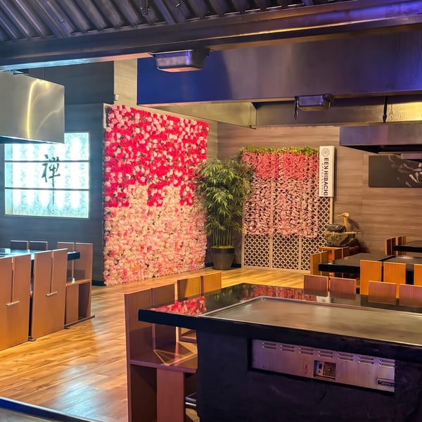Zen Hibachi restaurant interior featuring hibachi tables, vibrant pink floral walls, and a bamboo plant.