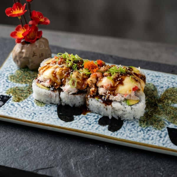 Sushi rolls with avocado, crab, sauce, and roe, on a decorative plate with a floral accent.