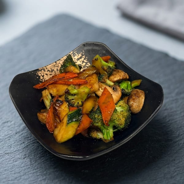 Sautéed vegetables, including broccoli, carrots, zucchini, and mushrooms, in a black and gold bowl.