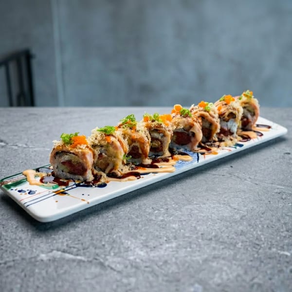 Eight sushi rolls with sauces, green onions, and orange roe on a decorative white plate.