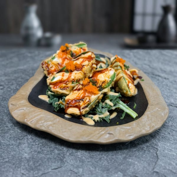 Fried jalapeño poppers topped with orange roe, drizzled with sauces, on a bed of greens.